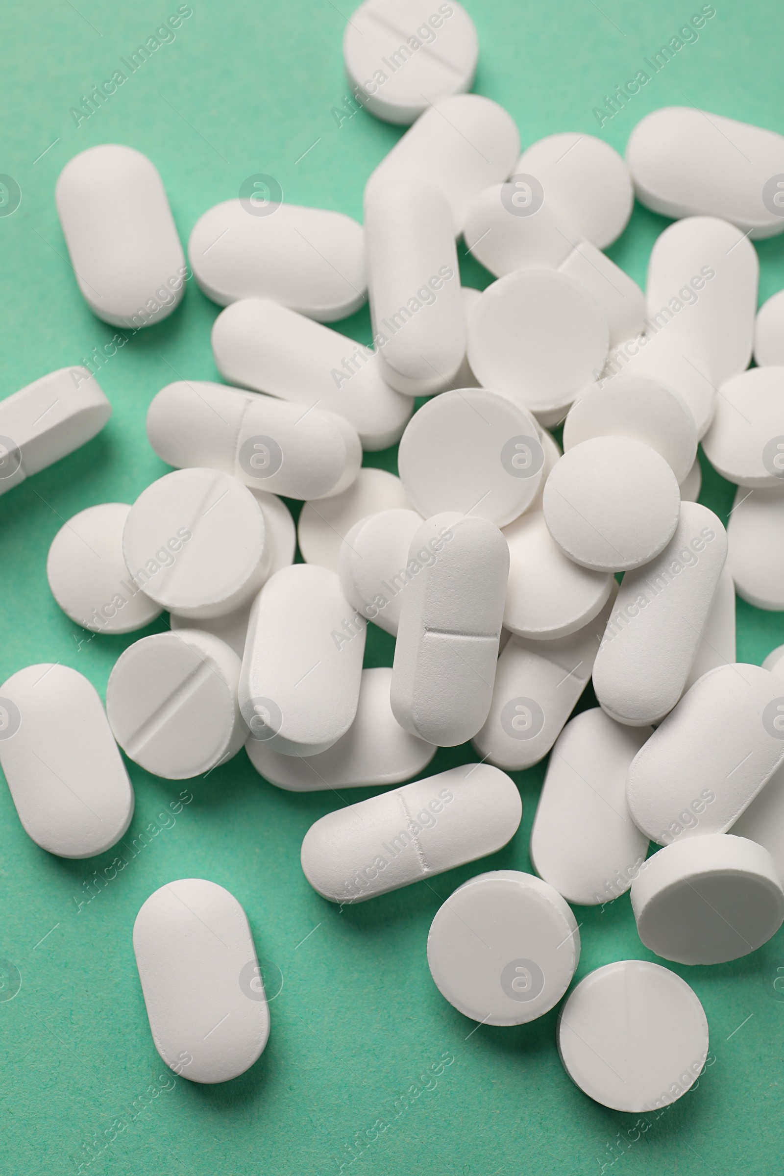 Photo of Pile of white pills on green background, flat lay