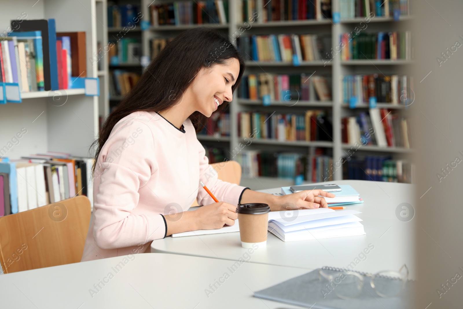 Photo of Young woman studying at table in library