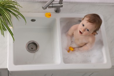 Photo of Cute little baby bathing in sink indoors, top view