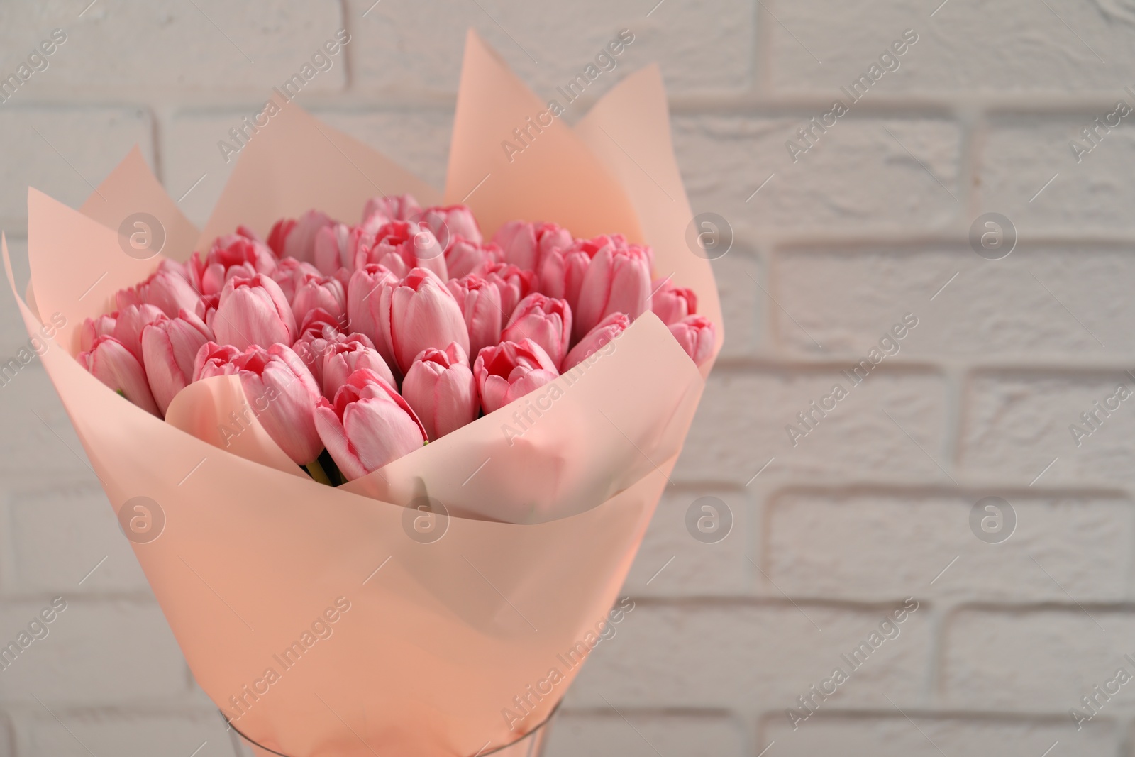 Photo of Bouquet of beautiful pink tulips near white brick wall, closeup. Space for text