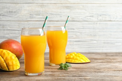 Photo of Fresh tropical mango juice, fruits and space for text on wooden table