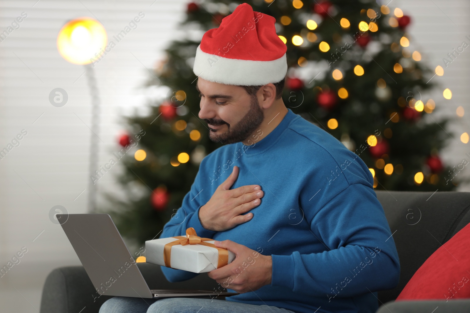 Photo of Celebrating Christmas online with exchanged by mail presents. Man thanking for gift during video call on laptop at home