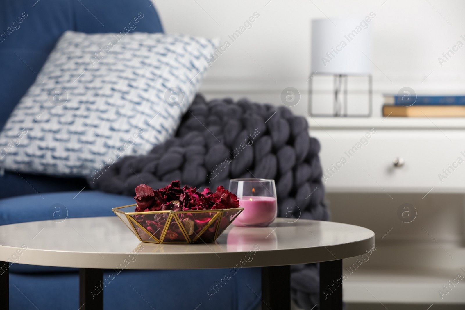 Photo of Aromatic potpourri of dried flowers in bowl and burning candle on table indoors