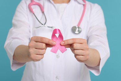 Photo of Mammologist with pink ribbon on light blue background, closeup. Breast cancer awareness