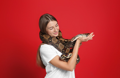 Young woman with boa constrictor on red background. Exotic pet