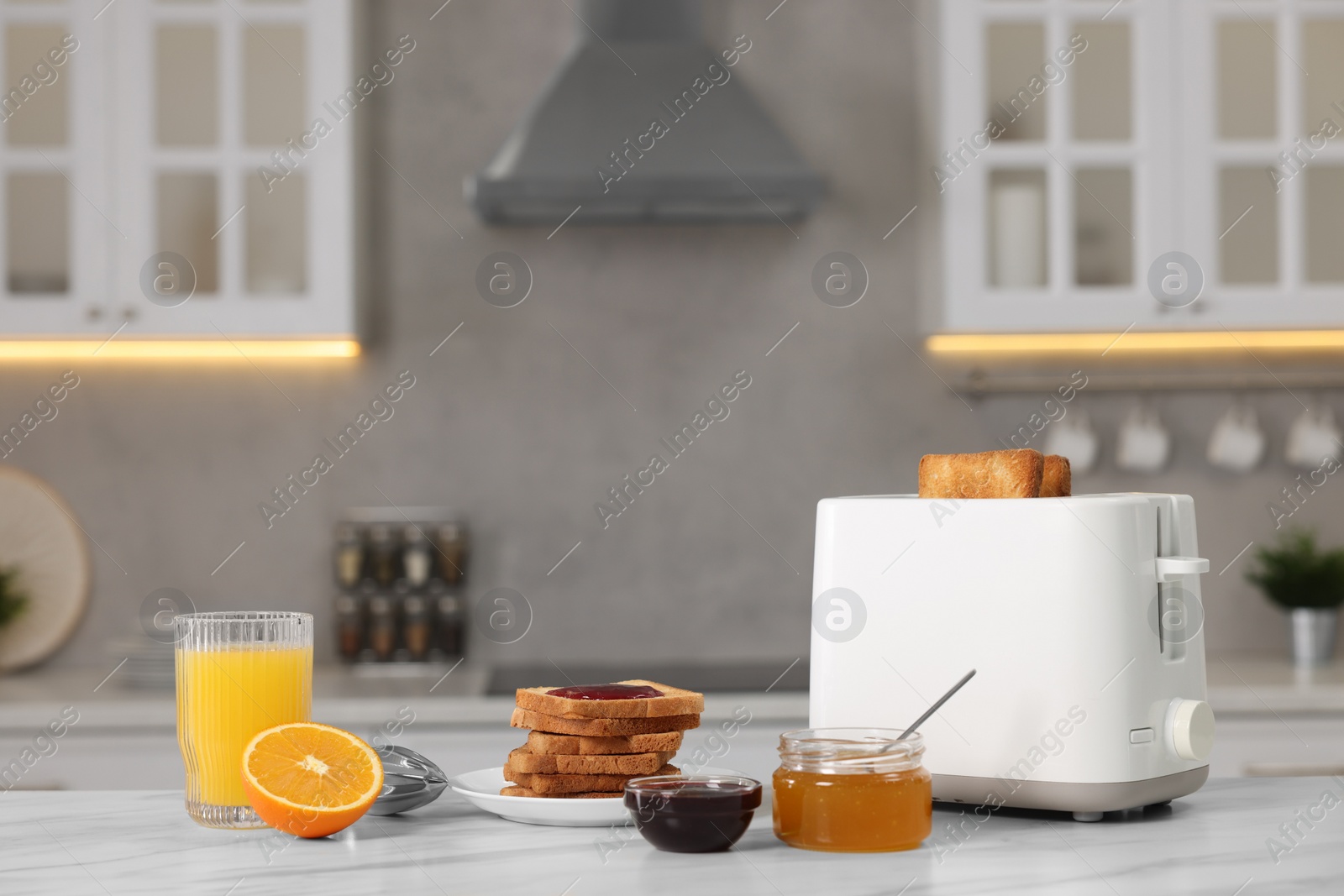 Photo of Making toasts for breakfast. Appliance, crunchy bread, honey, jam and orange fresh on white table in kitchen