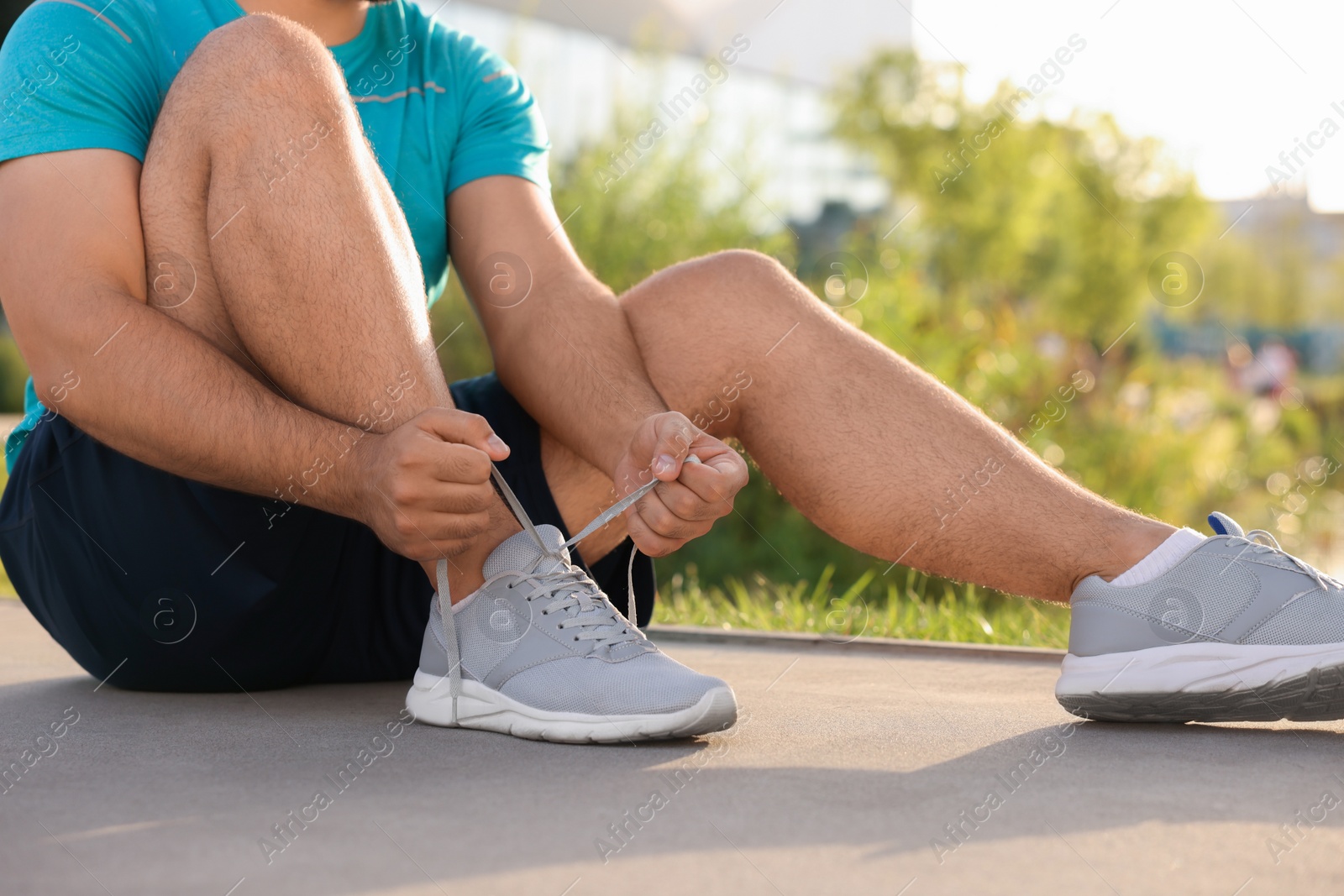 Photo of Man tying shoelaces before running outdoors on sunny day, closeup