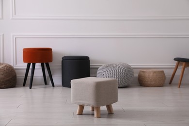 Photo of Different stylish poufs and ottomans near light wall