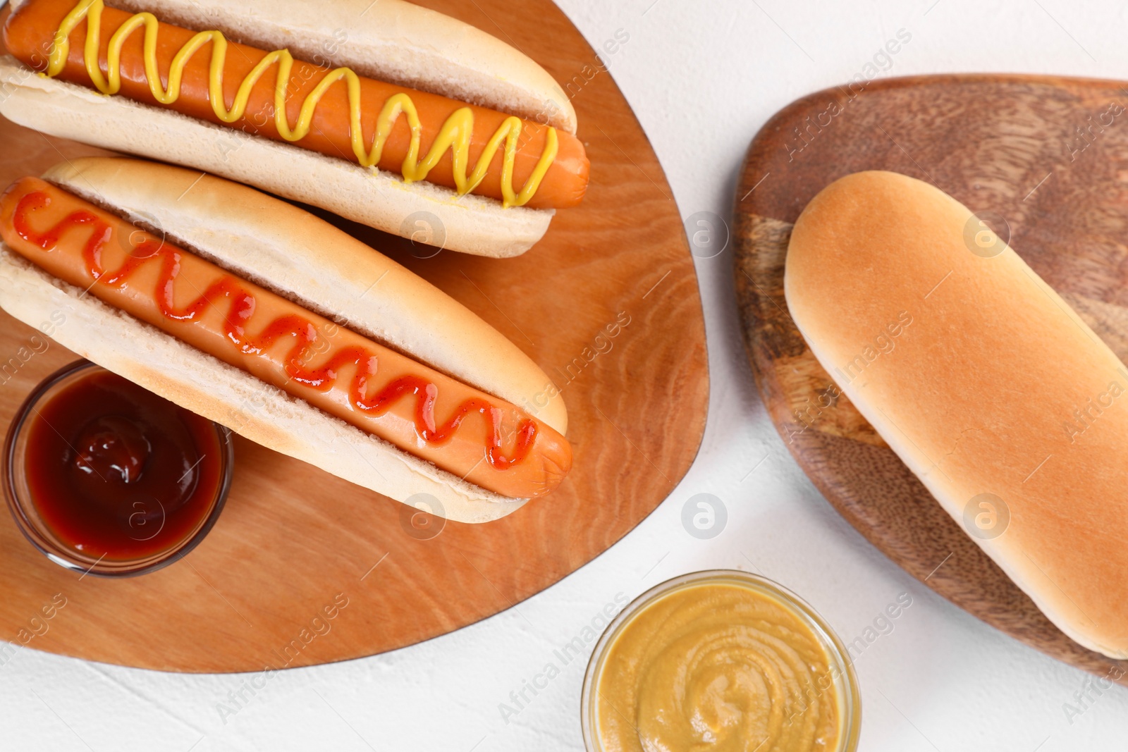 Photo of Tasty hot dogs with ketchup and mustard on white table, flat lay