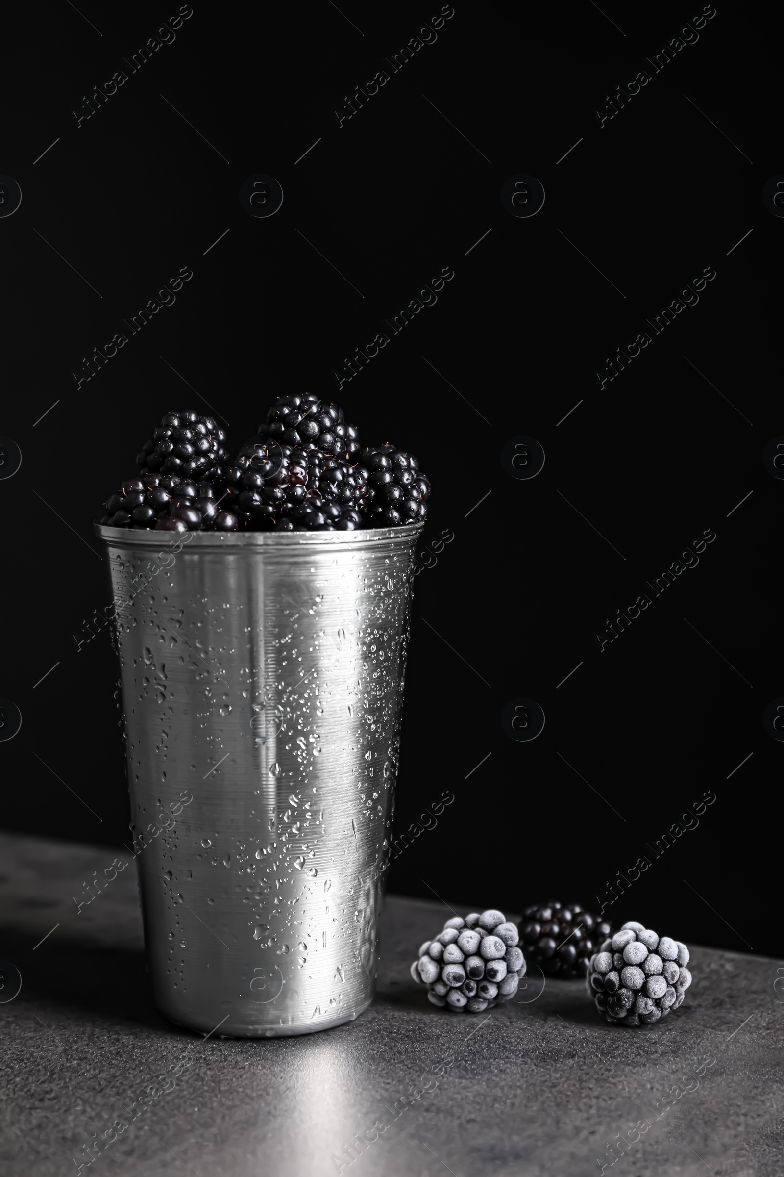 Photo of Fresh and frozen blackberries on grey table against dark background