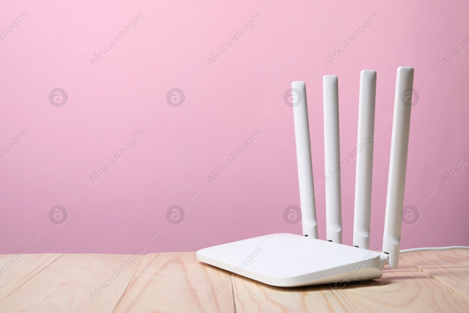 Photo of New Wi-Fi router on wooden table against pink background. Space for text