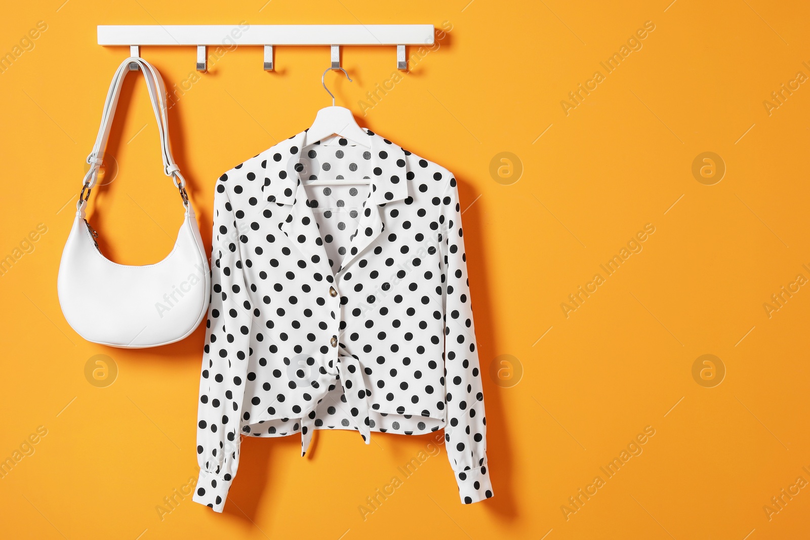 Photo of Hanger with polka dot shirt and bag on orange wall, space for text