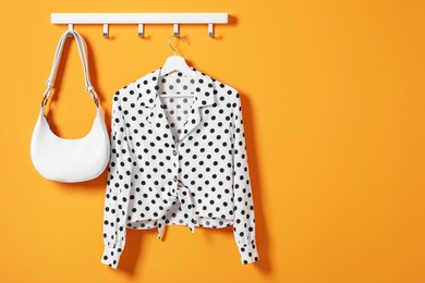 Photo of Hanger with polka dot shirt and bag on orange wall, space for text