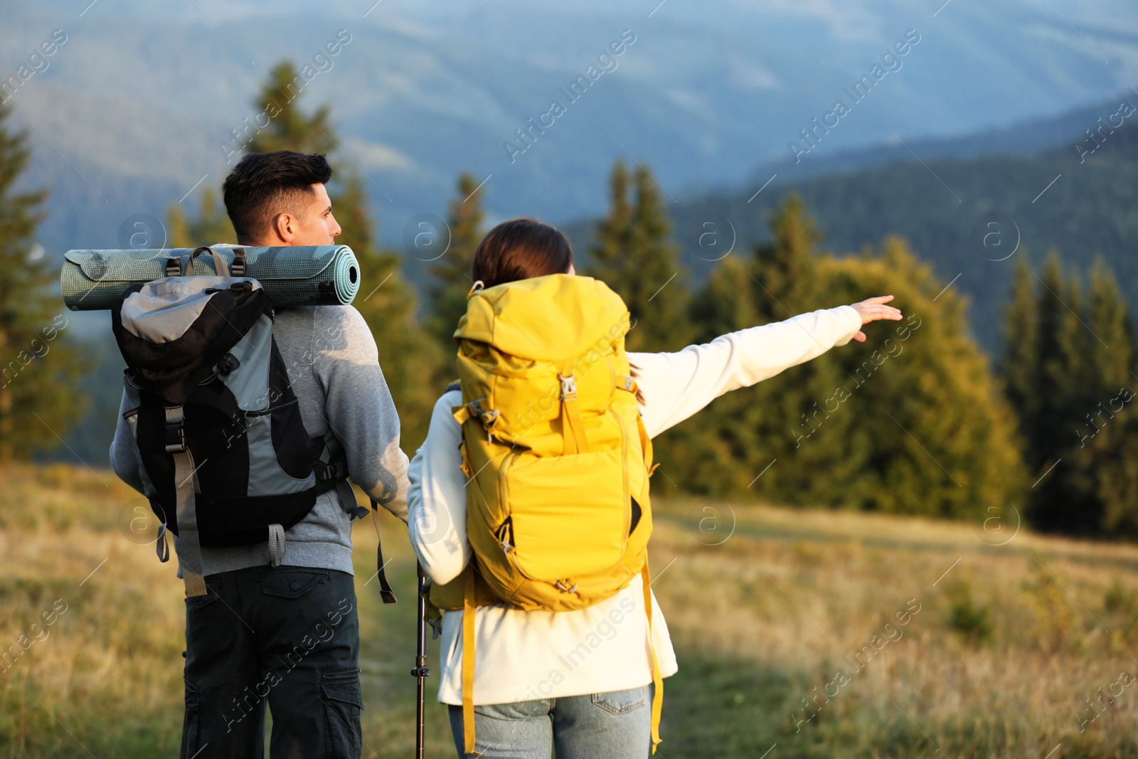 Photo of Couple with backpacks and trekking poles hiking in mountains, back view. Tourism equipment