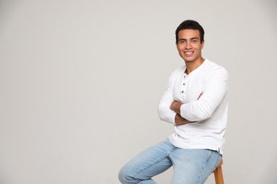 Handsome young African-American man sitting on stool against light background. Space for text