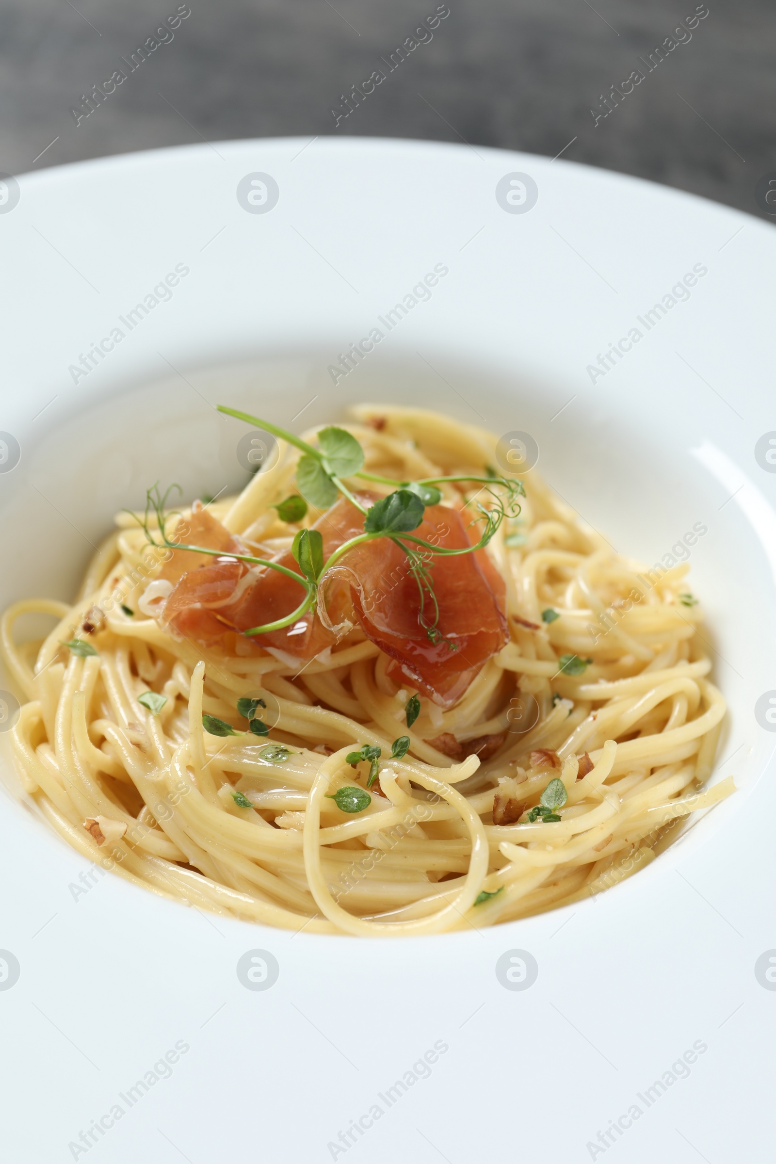 Photo of Tasty spaghetti with prosciutto and microgreens on plate, closeup. Exquisite presentation of pasta dish