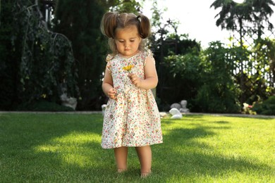 Photo of Cute little girl with flower walking on green grass in park