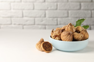 Bowl with tasty dried figs and green leaf on white wooden table. Space for text