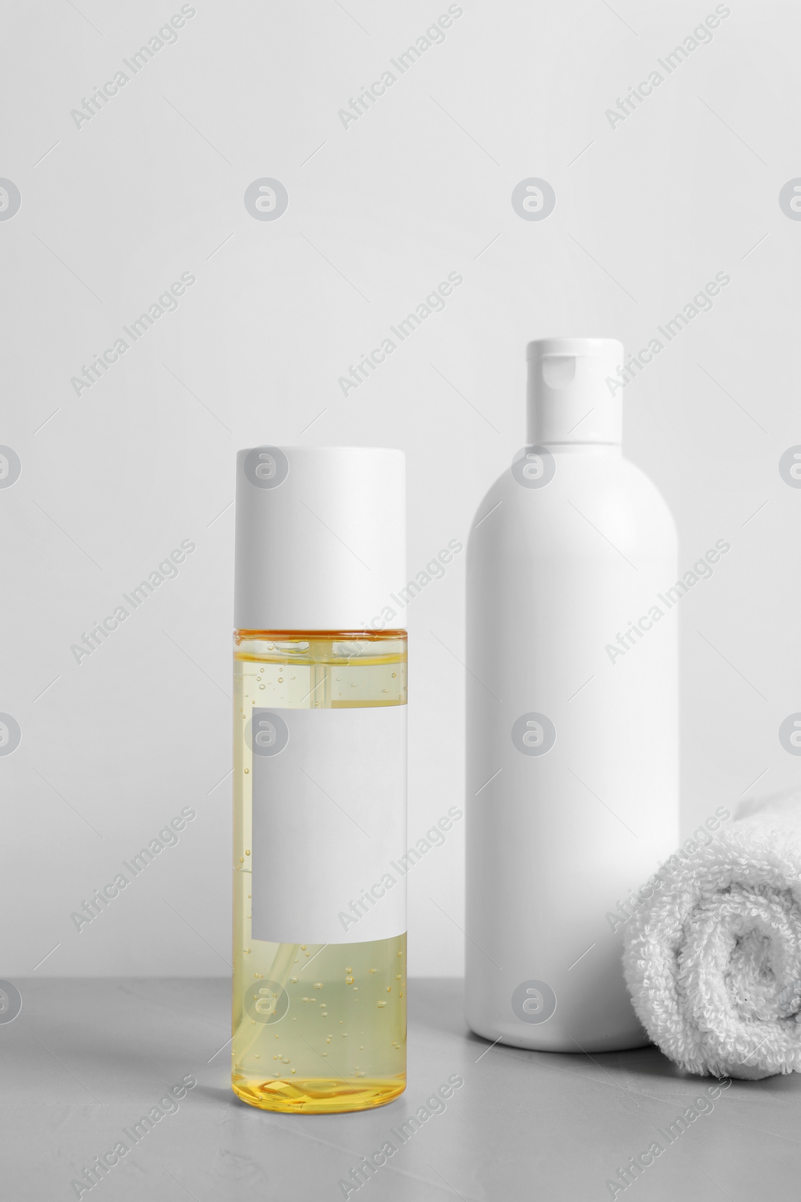 Photo of Bottles of cosmetic products and towel on grey table