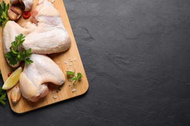Photo of Wooden board with fresh raw chicken wings and other products on black table, top view. Space for text