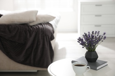 Photo of Beautiful lavender flowers, cup of coffee and book on white table indoors. Space for text
