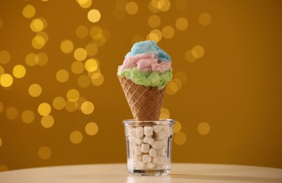 Photo of Sweet cotton candy in waffle cone on table against blurred lights