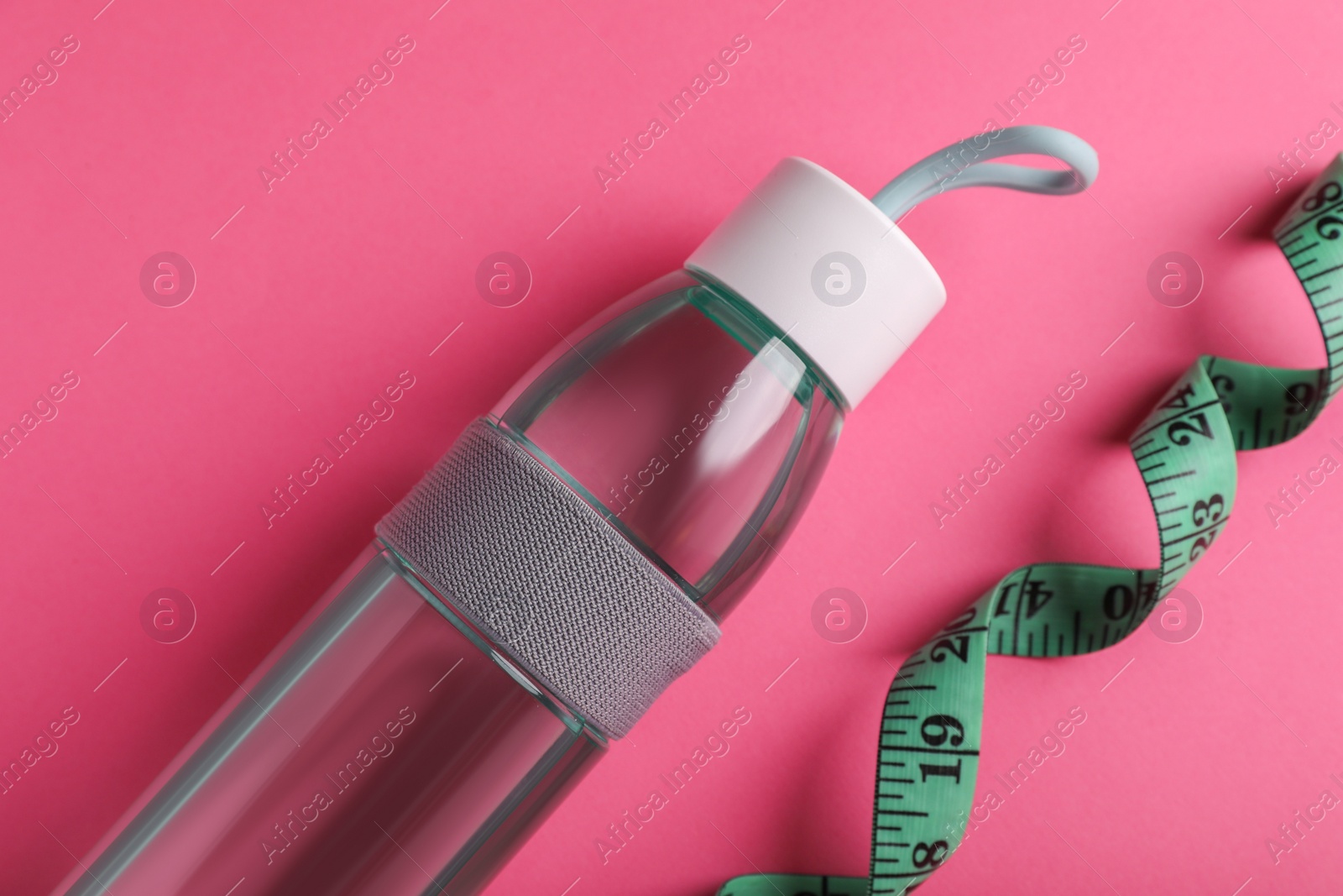 Photo of Measuring tape and bottle of water on pink background, flat lay. Weight control concept
