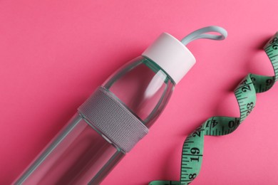 Photo of Measuring tape and bottle of water on pink background, flat lay. Weight control concept