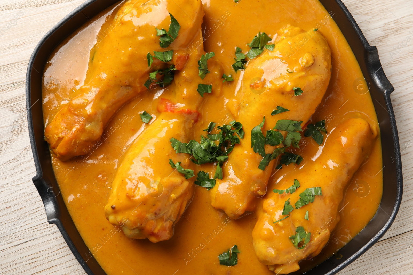 Photo of Tasty chicken curry with parsley on wooden table, top view