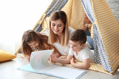 Nanny and little children reading book in tent at home