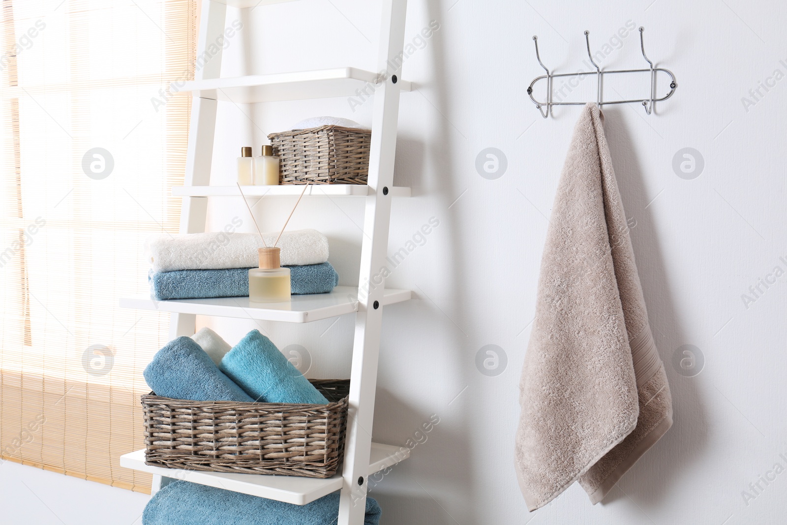 Photo of Shelving unit and rack with clean towels and toiletries near white wall