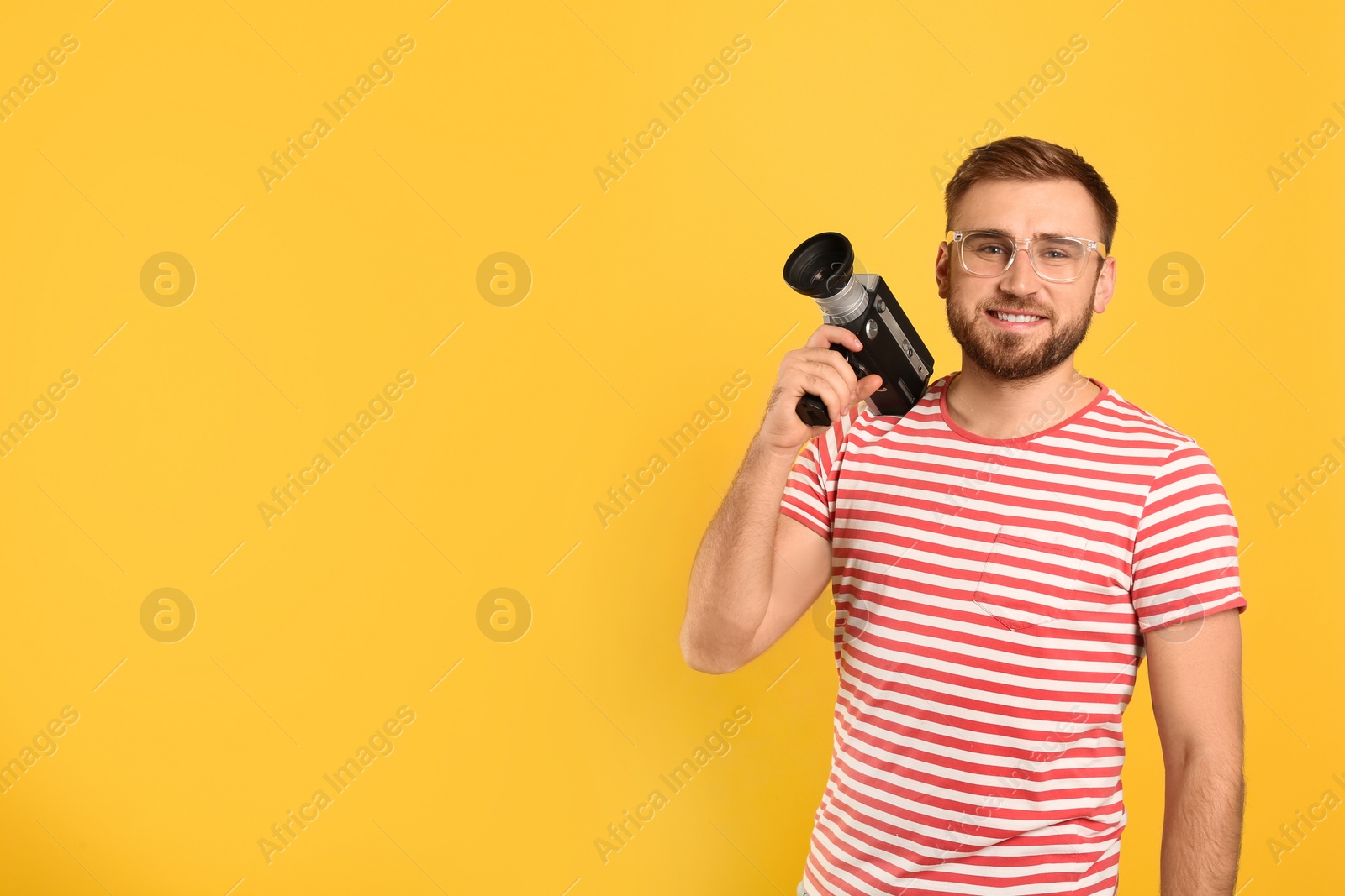 Photo of Young man with vintage video camera on yellow background, space for text