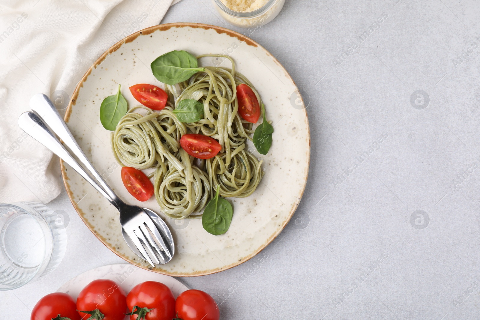 Photo of Tasty pasta with spinach and tomatoes served on light grey table, flat lay. Space for text