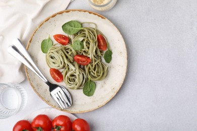 Tasty pasta with spinach and tomatoes served on light grey table, flat lay. Space for text