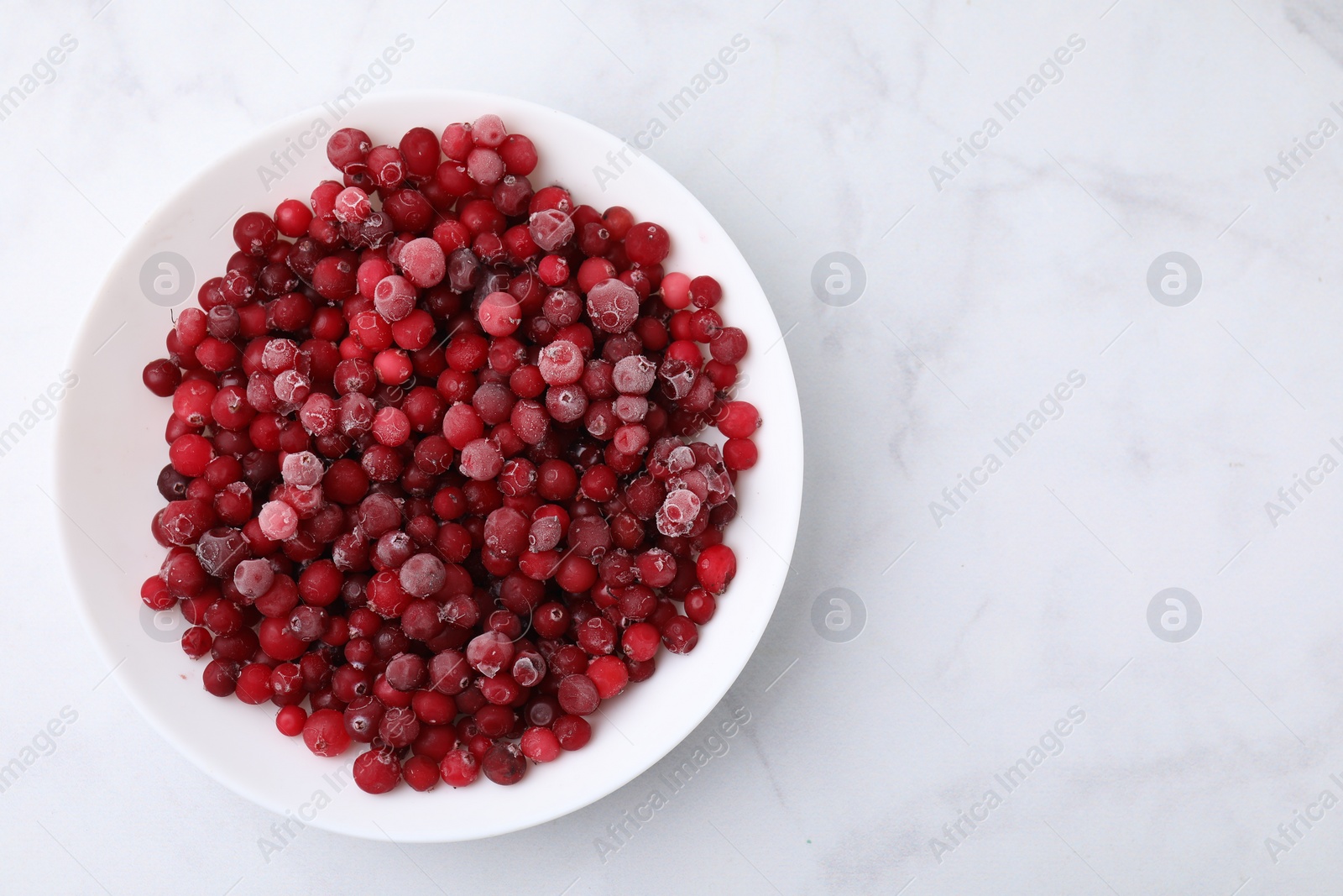 Photo of Frozen red cranberries in bowl on white marble table, top view. Space for text