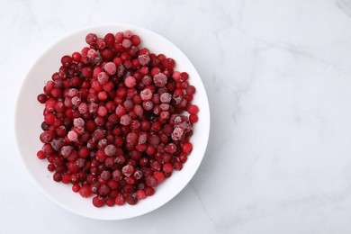 Frozen red cranberries in bowl on white marble table, top view. Space for text