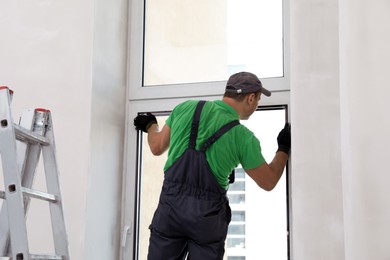 Photo of Worker in uniform installing double glazing window indoors, back view