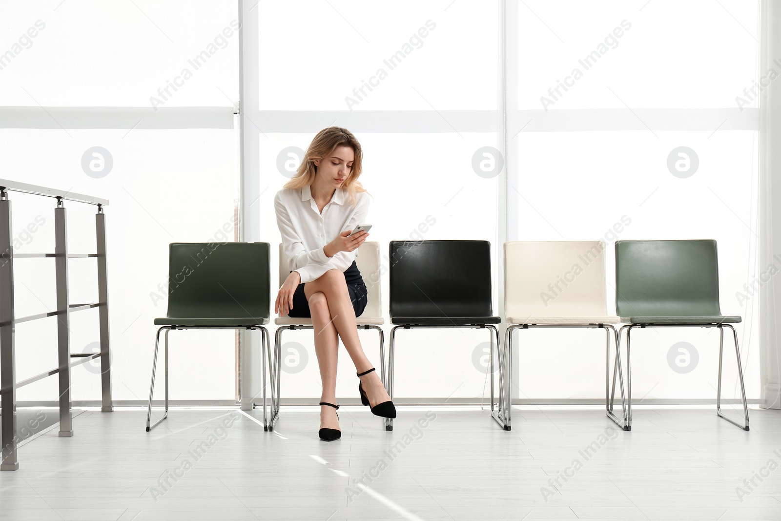 Photo of Young woman with smartphone waiting for job interview in office hall