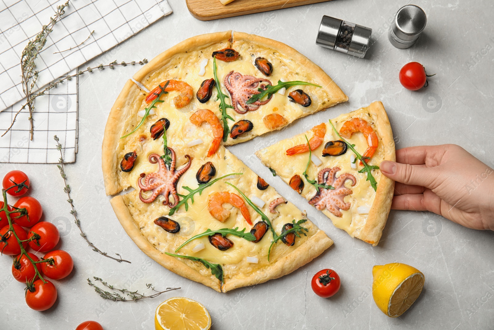 Photo of Woman taking piece of delicious seafood pizza at grey marble table, top view