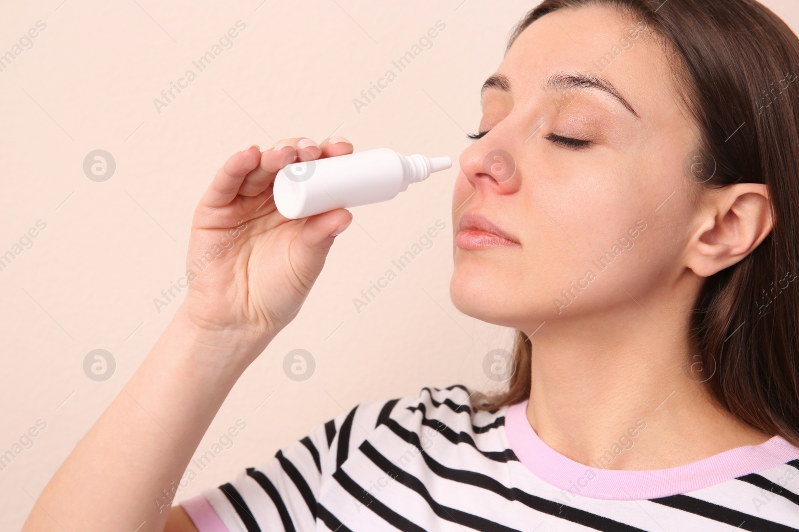 Photo of Woman using nasal spray on beige background