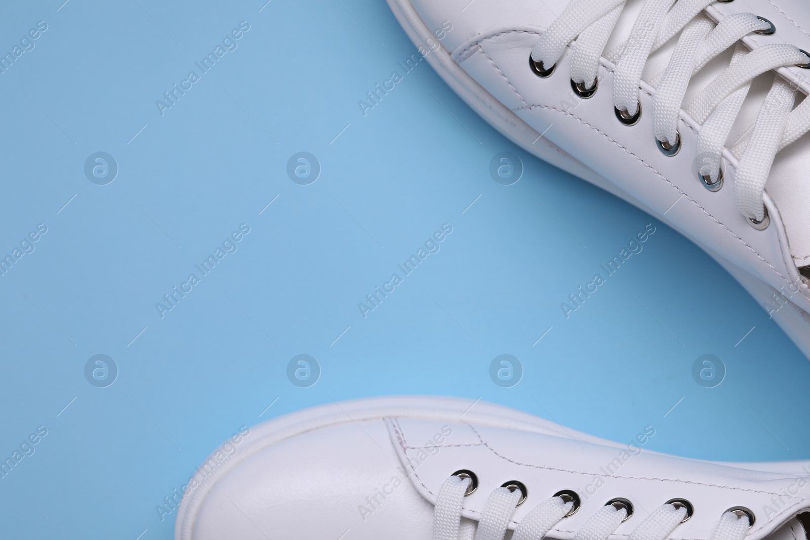 Photo of Pair of stylish white sneakers on light blue background, top view. Space for text