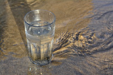 Photo of Glass of clean water on wet sand outdoors. Space for text