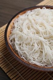 Bowl with cooked rice noodles and straw mat on table, closeup