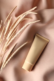 Photo of Tube of skin foundation and decorative plants on beige fabric, flat lay. Makeup product