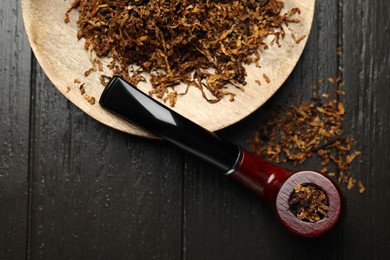 Photo of Smoking pipe and dry tobacco on dark wooden table, flat lay