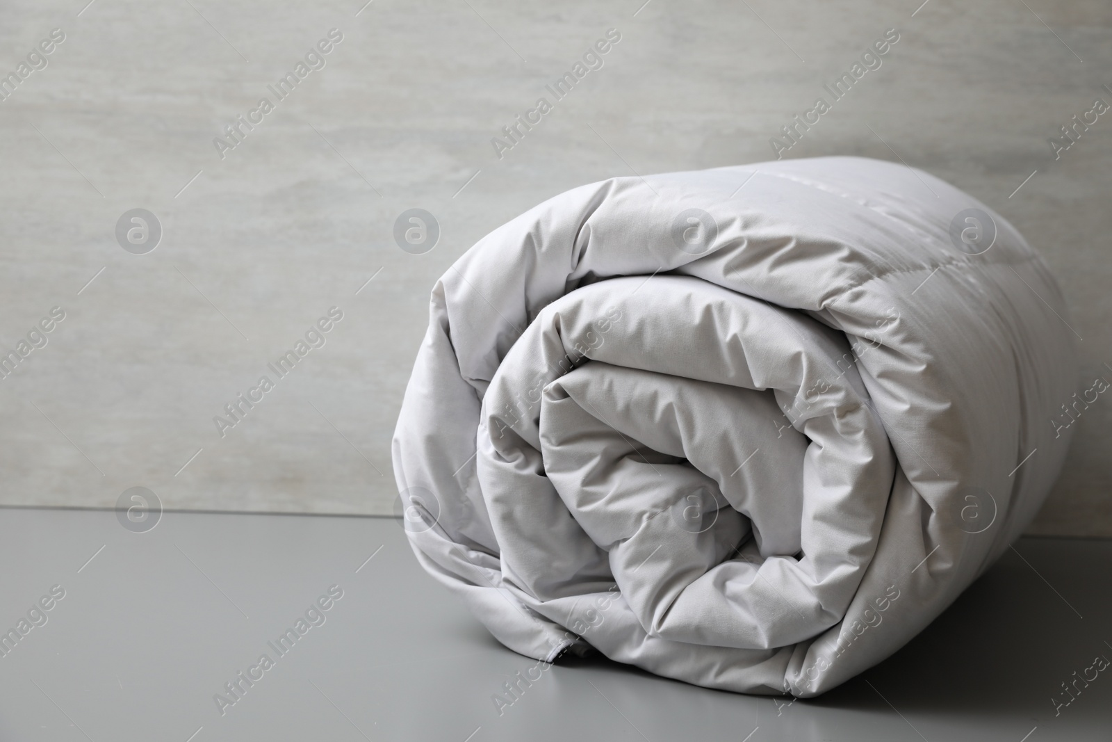 Photo of Soft rolled blanket on light grey table, closeup