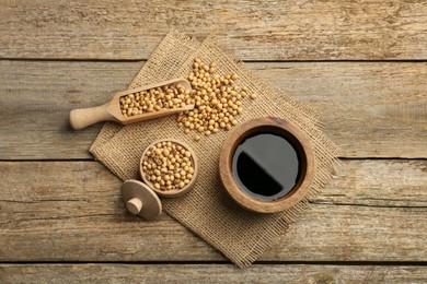 Photo of Soy sauce in bowl and soybeans on wooden table, flat lay