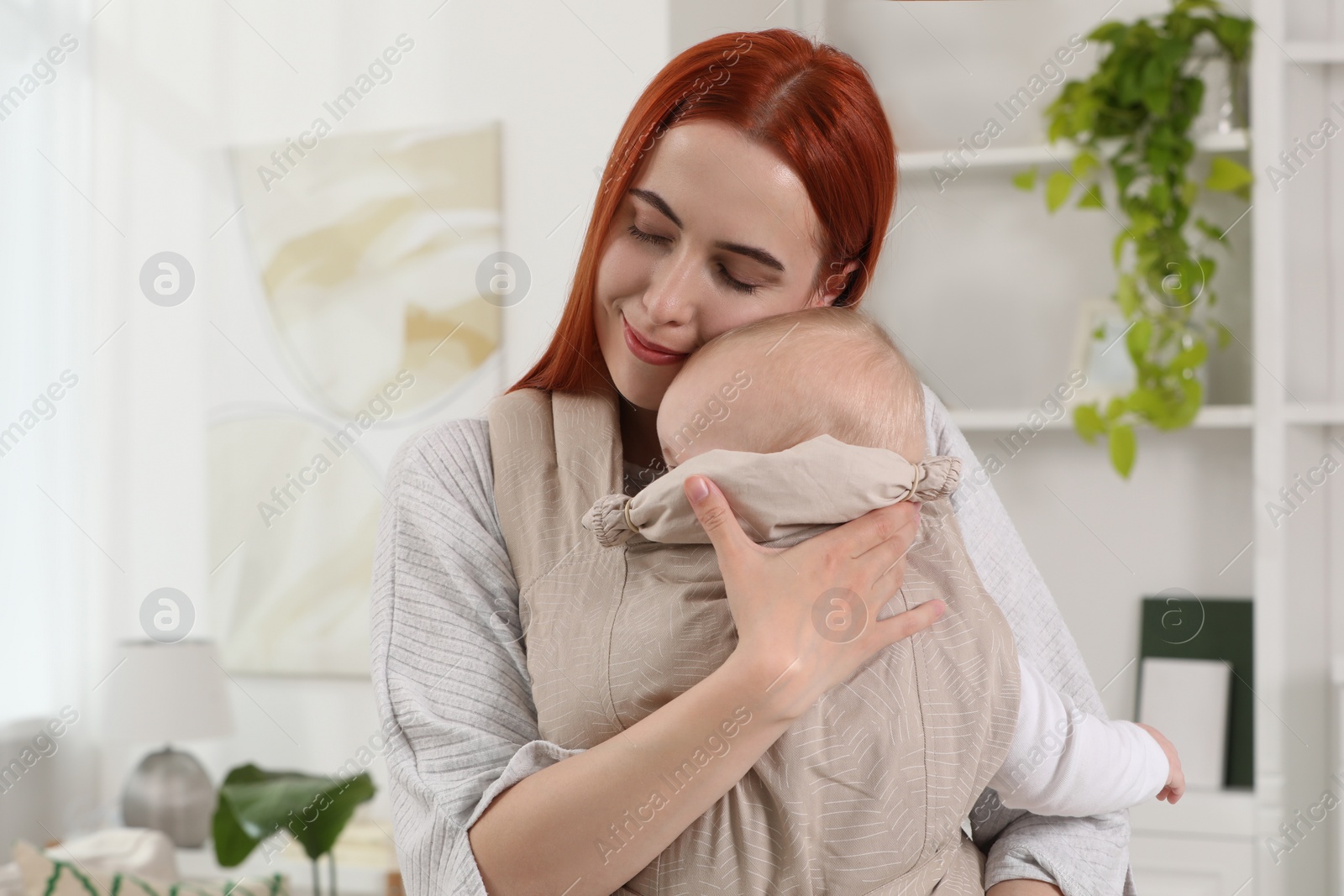 Photo of Mother holding her child in sling (baby carrier) at home