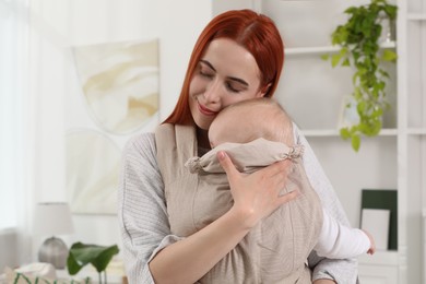 Mother holding her child in sling (baby carrier) at home