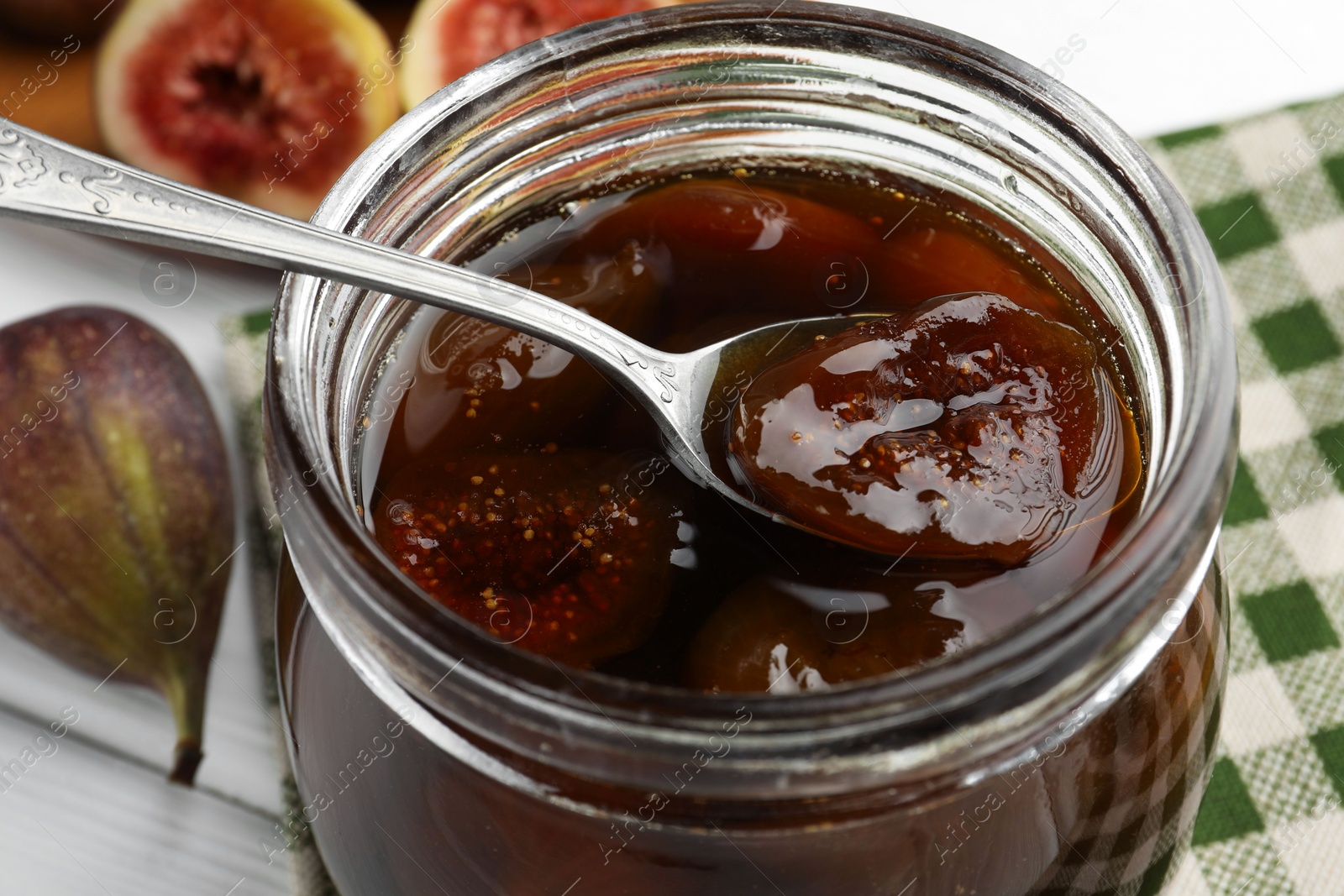 Photo of Jar of tasty sweet fig jam on white table, closeup